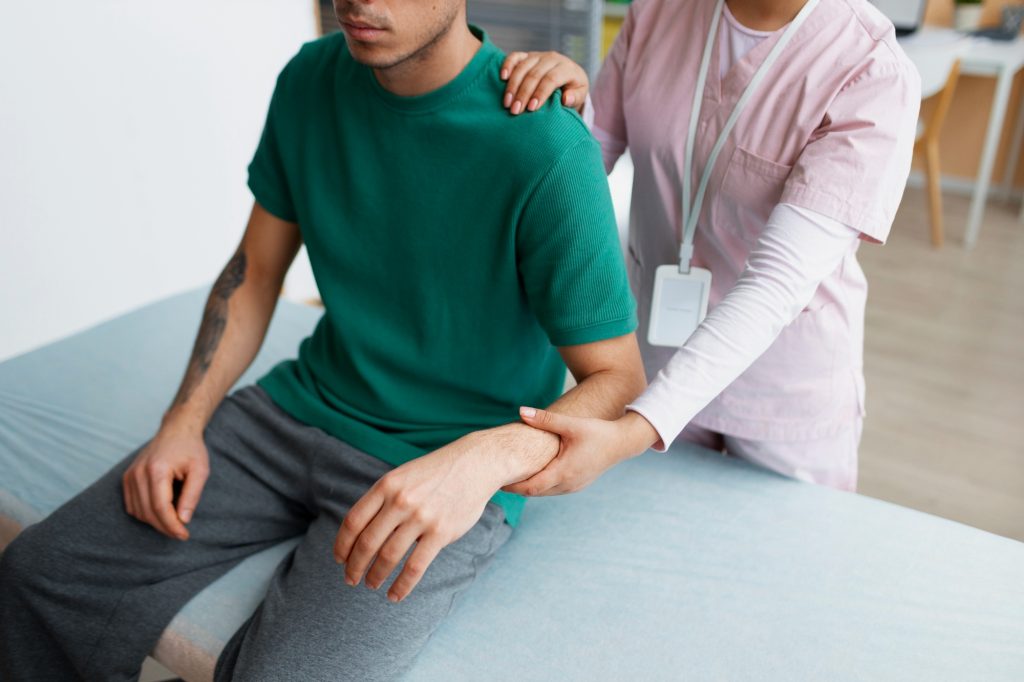 A physical therapist gently examining a male patient's arm and elbow joint on a treatment table.