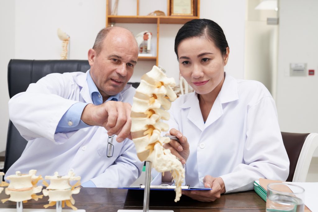 A medical professional reviewing a spinal X-ray or MRI while discussing a guided cortisone injection procedure with a patient.