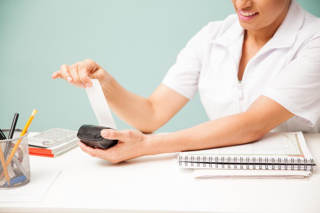 A clinic receptionist processing a payment and printing a receipt from a card terminal.