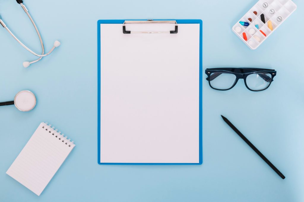 A top-down view of a medical clipboard, stethoscope, and pill organizer, representing a customized patient recovery protocol.