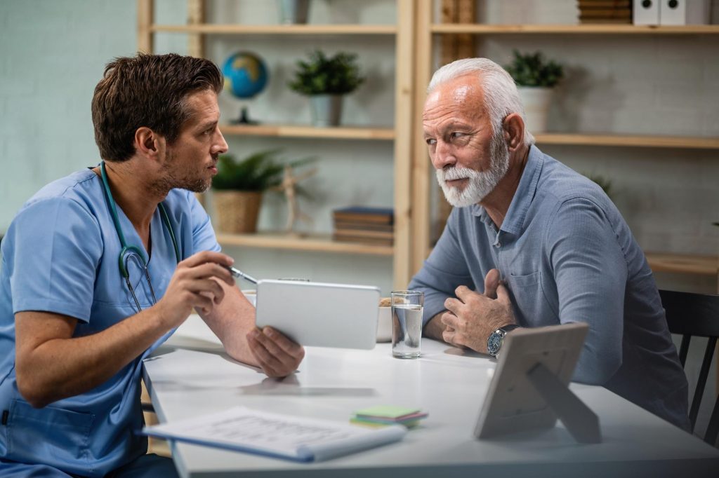 A compassionate orthopedic doctor in blue scrubs consulting with a senior male patient, reviewing a personalized treatment plan on a tablet.
