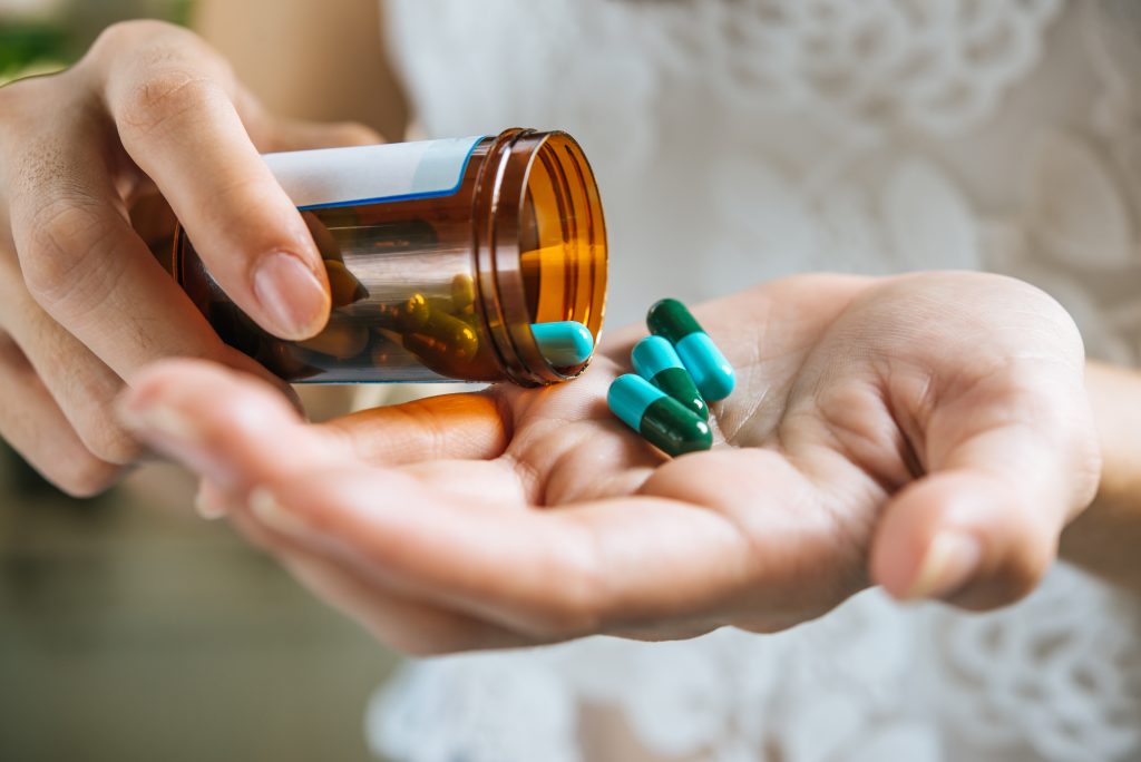 A close-up of a woman's hand pouring white medicinal pills out of a brown prescription bottle.
